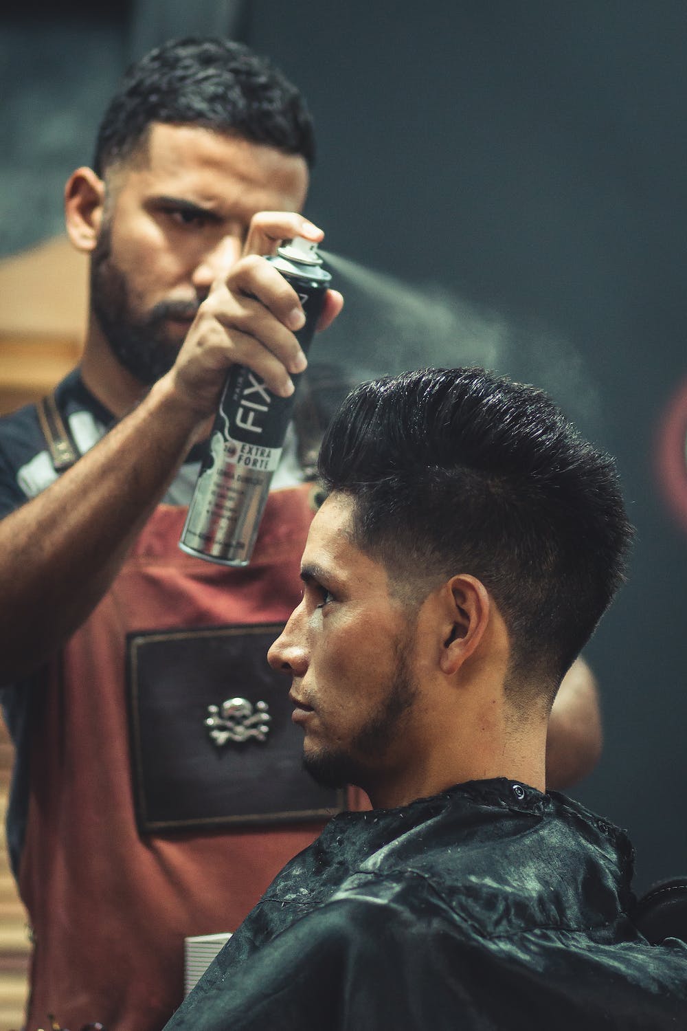 Barber spraying gel into customers freshly cut hair to maintain shape of design